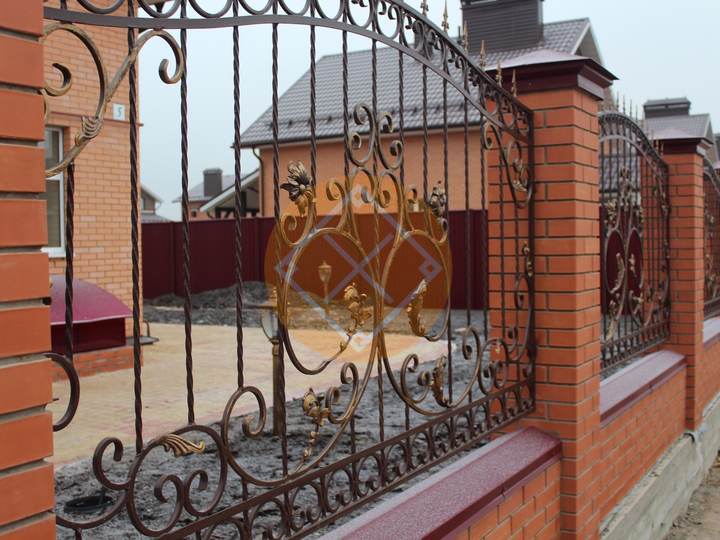 кованый забор с кирпичными столбами и отливами на цокольной ленте